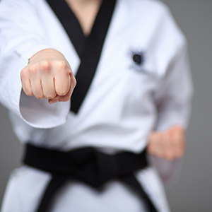 A young black belt man who is practicing karate by punching a fist in the air.