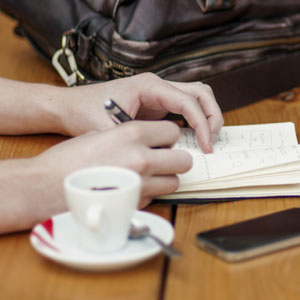 Young lady at a coffee shop having an espresso and writing in her journal.