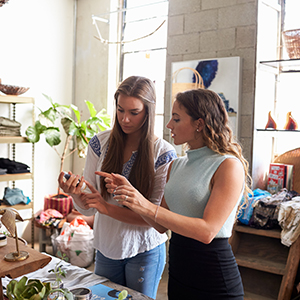 Two young millennial girls at a store helping each other make a selection.