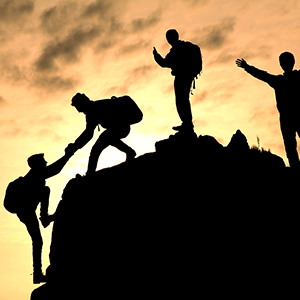 A teammate is helping the last person to climb up the mountain to reach their goal.