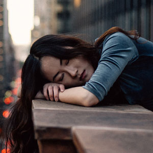 An overworked and tired young lady is taking a quick nap on the side of her office building.